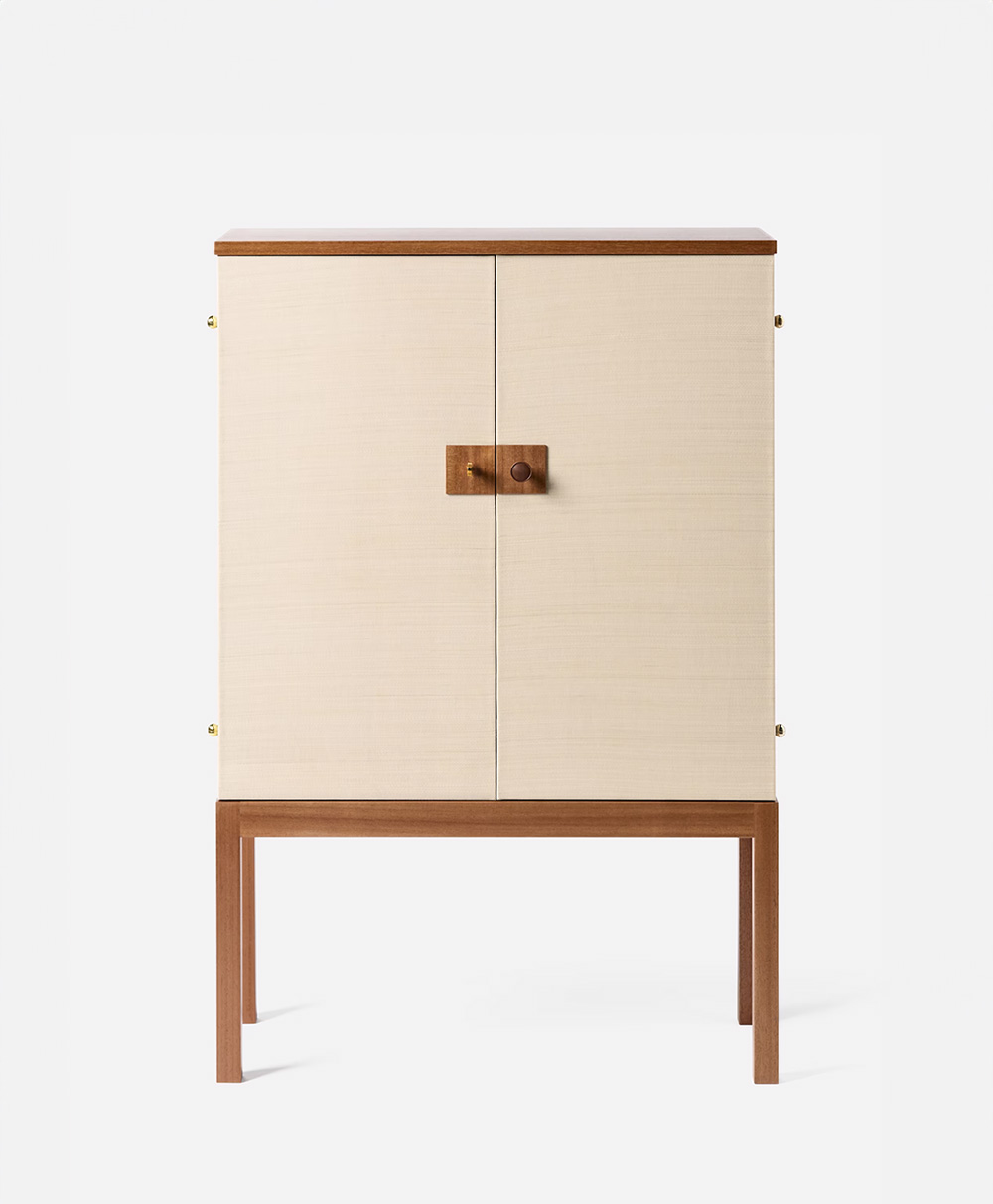 A minimalist cabinet with light beige doors and a wooden frame, featuring a square wooden handle in the center and standing on four slender wooden legs against a white background.