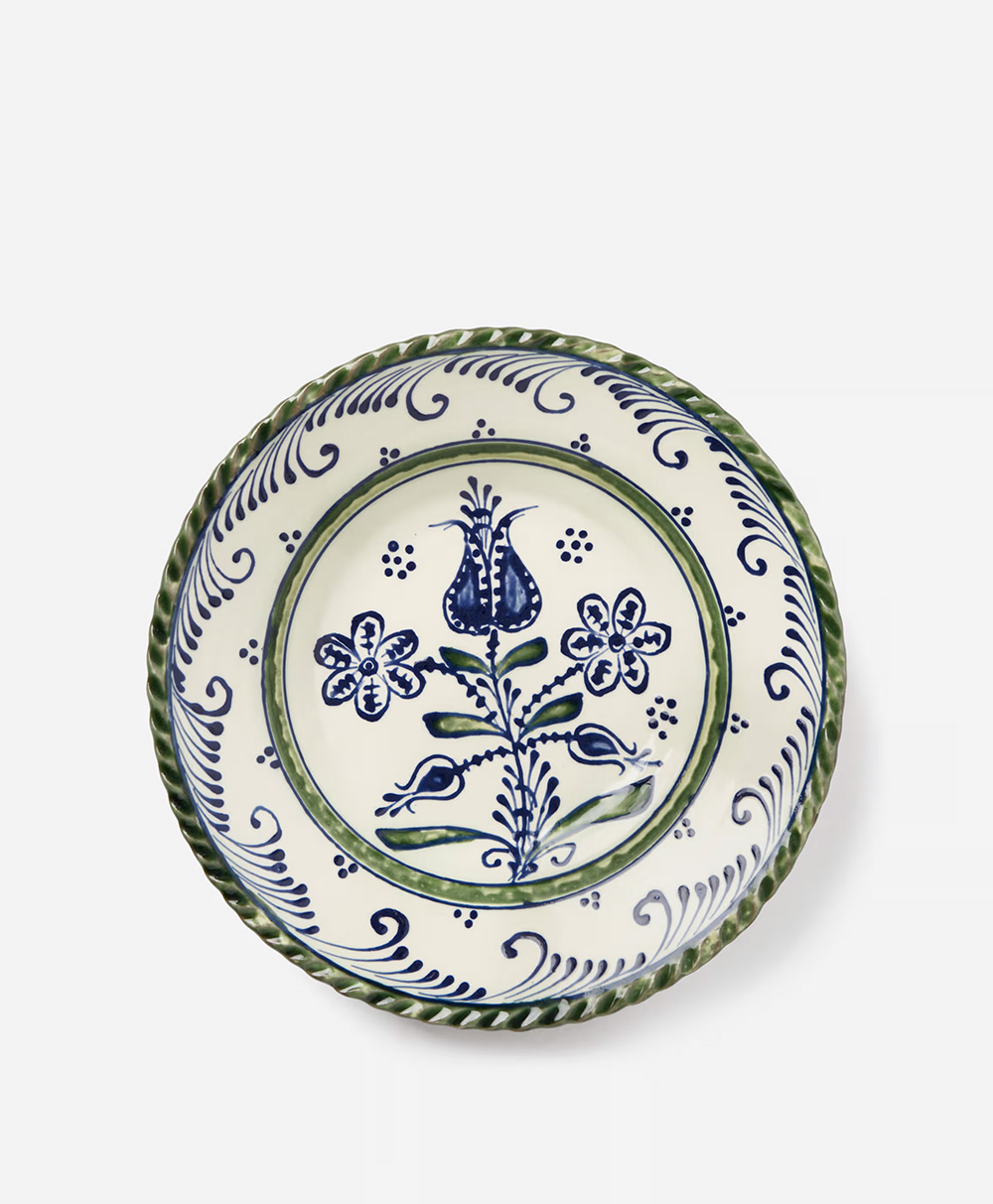 A decorative ceramic plate with a blue and green floral pattern, featuring a central tulip and two flowers, bordered by a green and blue swirling design.