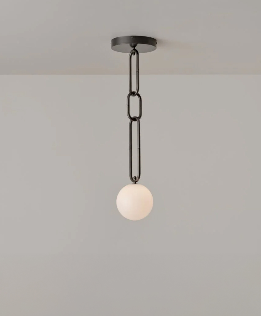A modern ceiling pendant light with a matte black chain and a round white glass globe, hanging against a plain light gray wall.