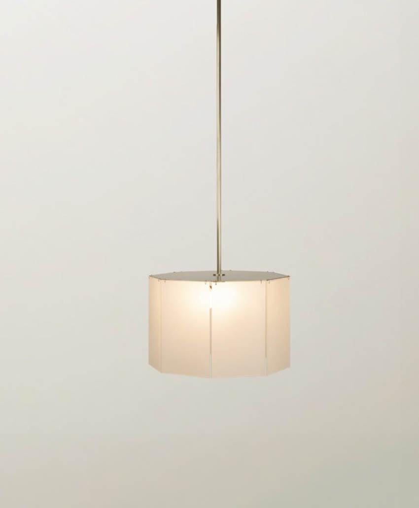 A modern pendant light with a white, octagonal lampshade hangs from a thin metal rod against a plain light gray background. The lamp is softly illuminated.