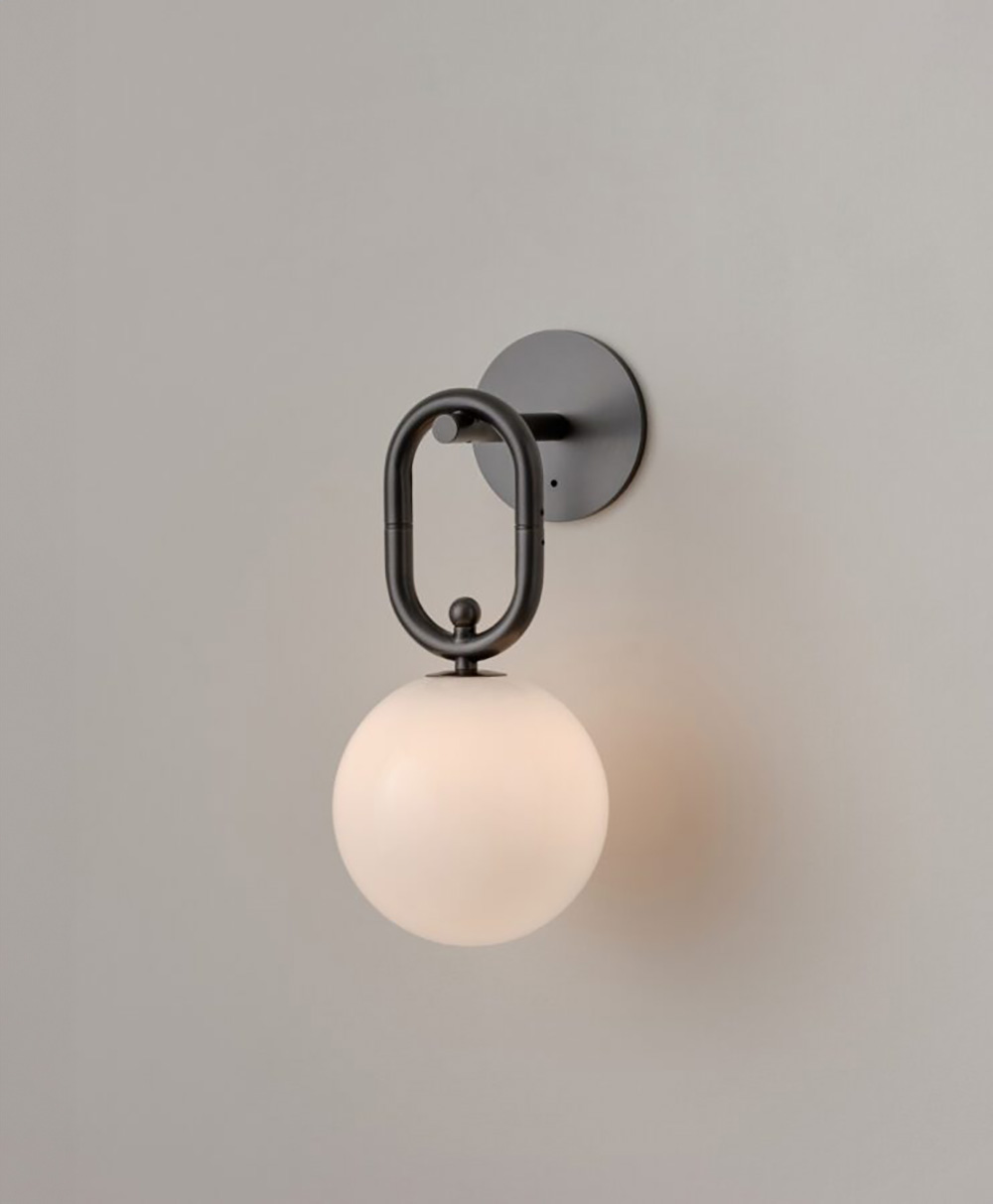 A modern wall sconce with a round black metal base and an oval frame holding a white frosted glass globe, mounted on a plain light gray wall.