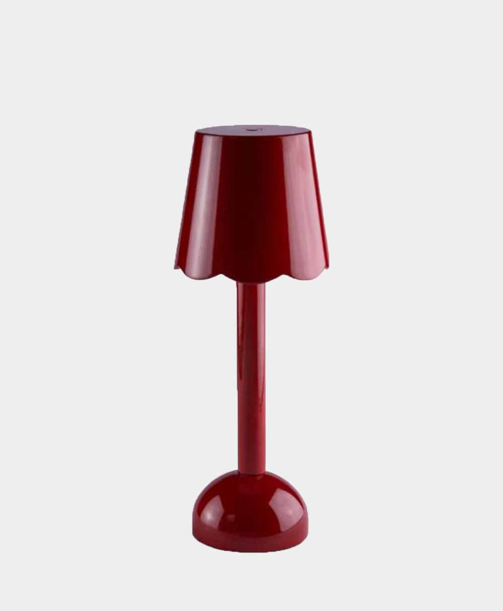 A red table lamp with a glossy finish, featuring a scalloped lampshade and a rounded base, displayed against a plain light gray background.