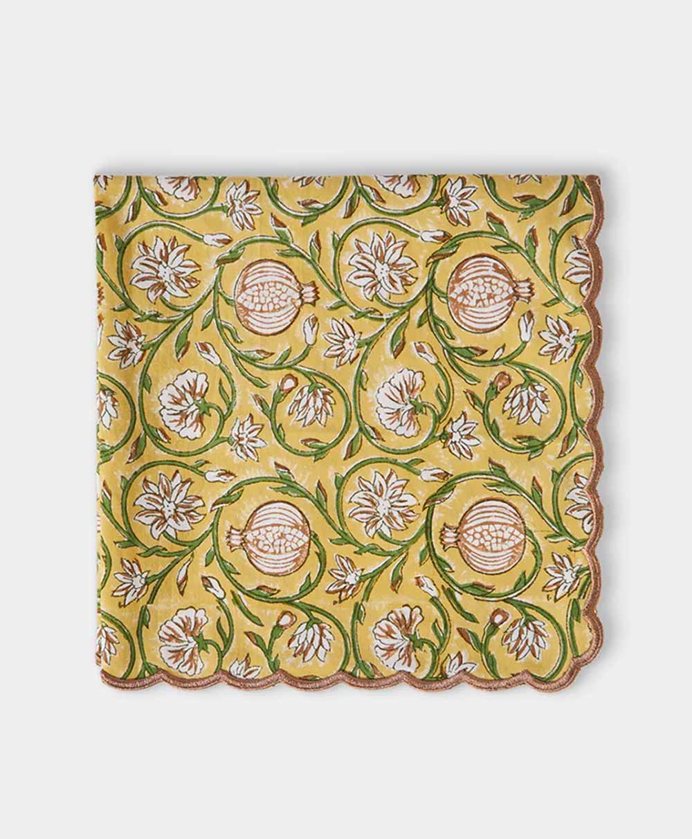A yellow cloth napkin with a scalloped edge, decorated with a floral and fruit pattern in green, brown, and white tones.