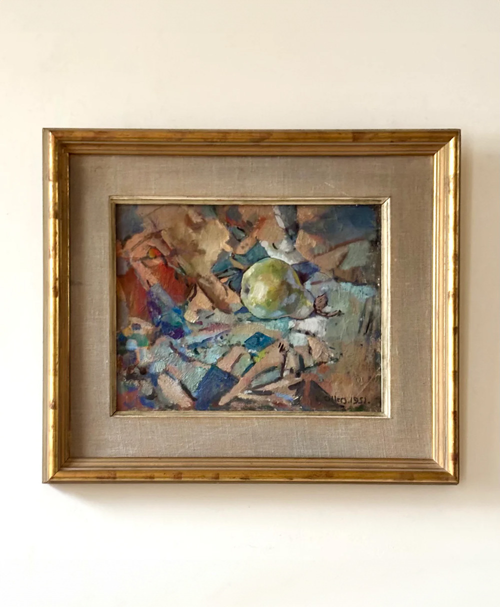 A framed abstract painting featuring a mix of earthy tones and vibrant colors with a green sphere at the center, displayed on a plain white wall.