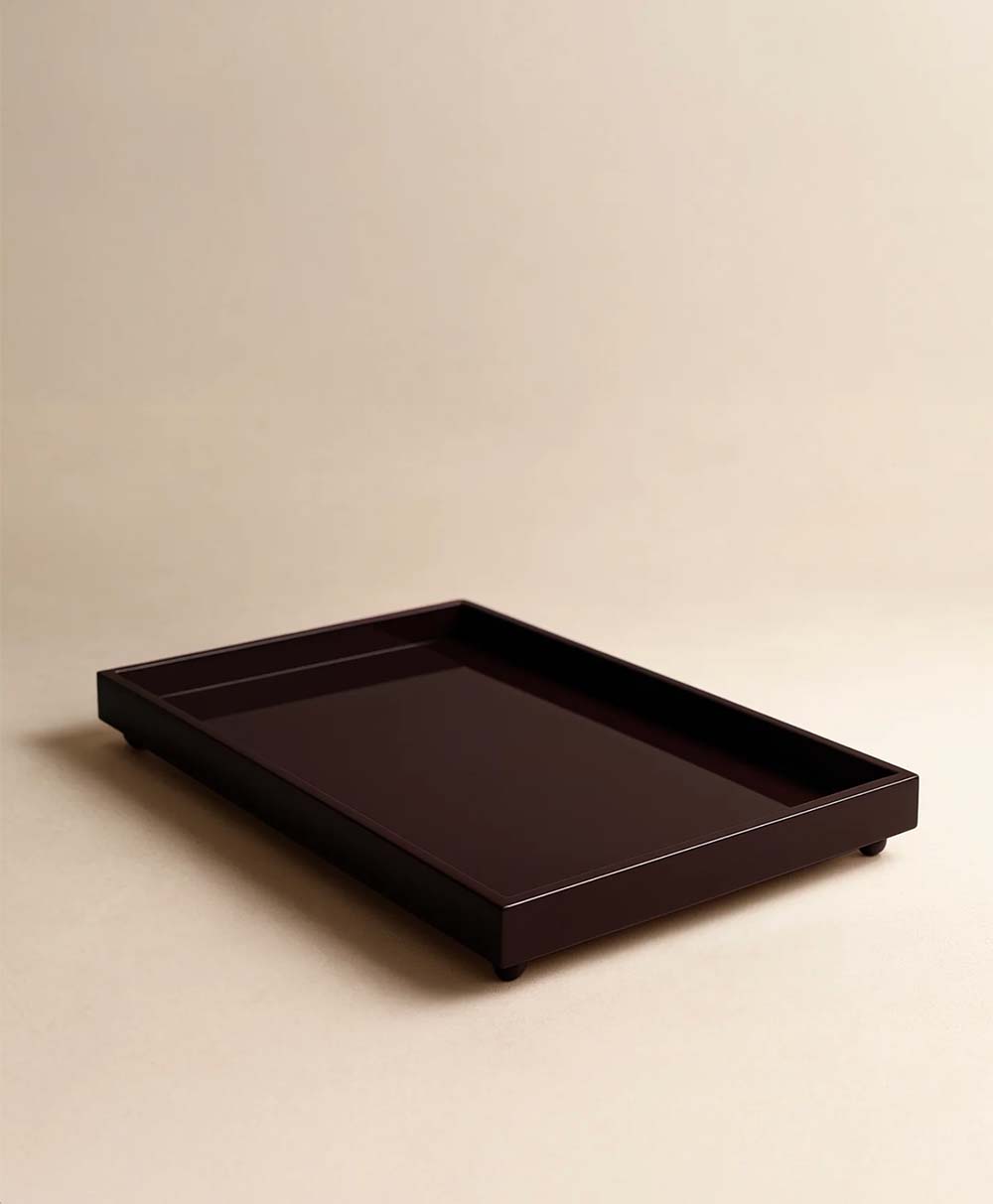 A rectangular, dark brown tray with short sides and small legs, placed on a light beige surface against a matching background.