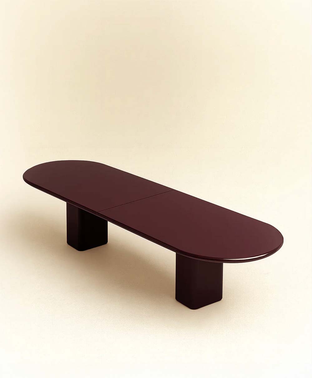 A modern, minimalist dark brown oval table with thick rectangular legs, set against a plain, light beige background.