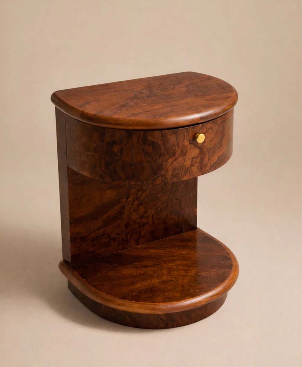 A small, vintage wooden nightstand with a rich brown finish, rounded edges, an upper drawer with a gold knob, and a lower open shelf, set against a neutral background.