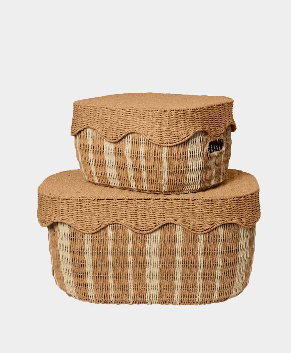 Two woven baskets with lids, one stacked on top of the other. Both baskets are tan with lighter vertical stripes and scalloped edges on the lids. The background is plain white.