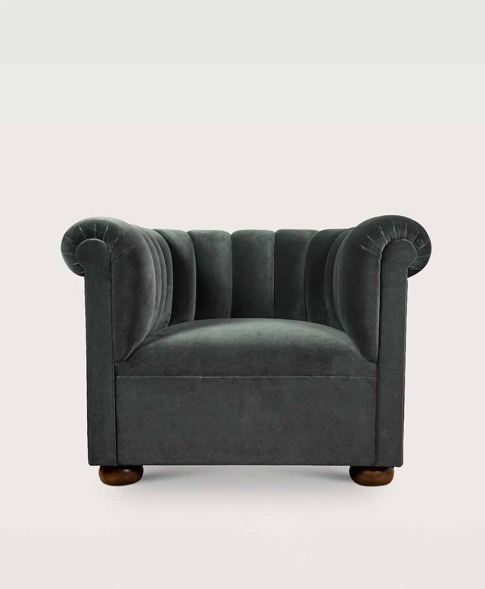 A plush, dark gray velvet armchair with rolled arms, deep tufted backrest, and rounded wooden feet, set against a plain white background.