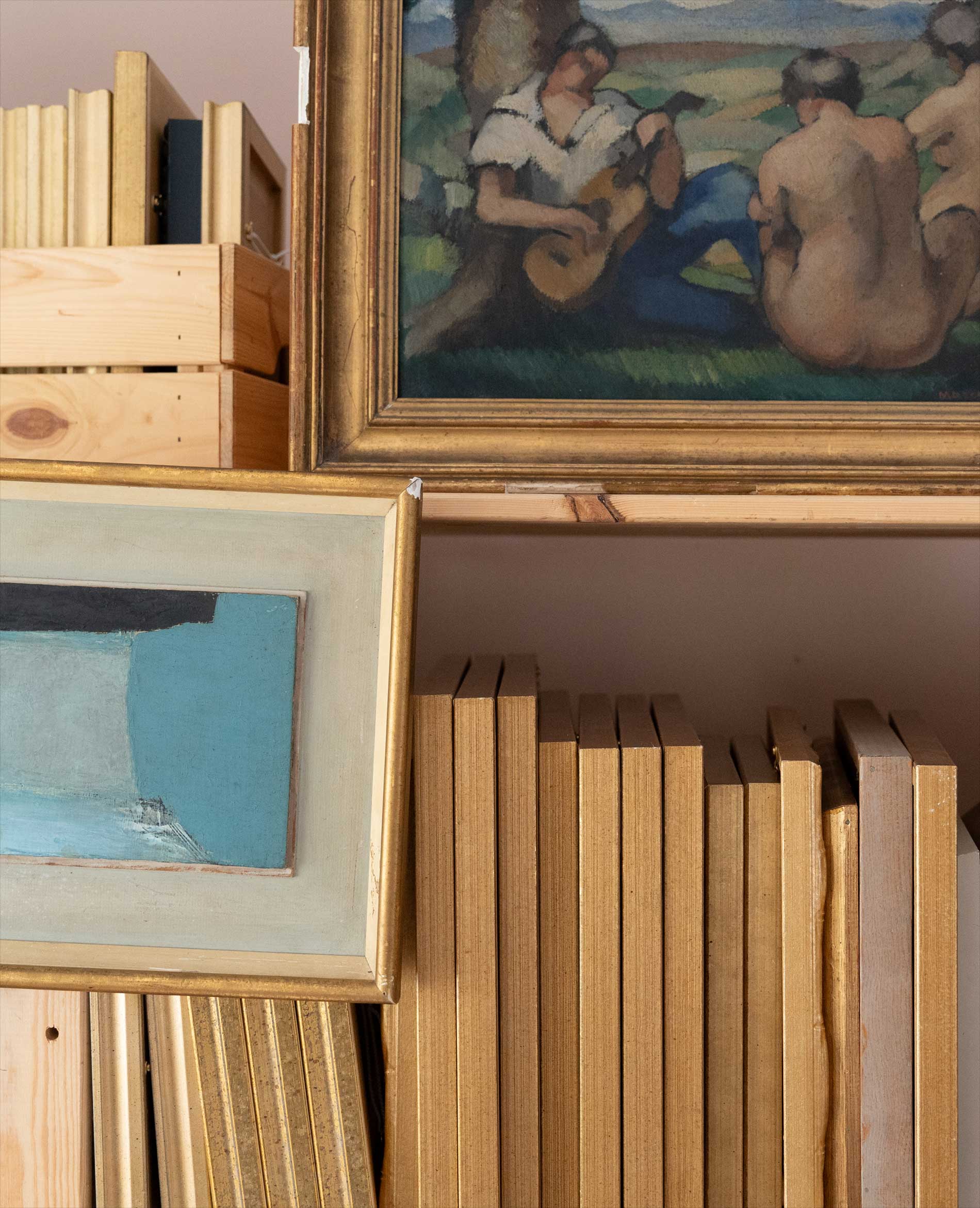 Framed paintings and numerous beige-covered books are arranged on wooden shelves, with one painting depicting seated figures and another featuring abstract art in blue tones.