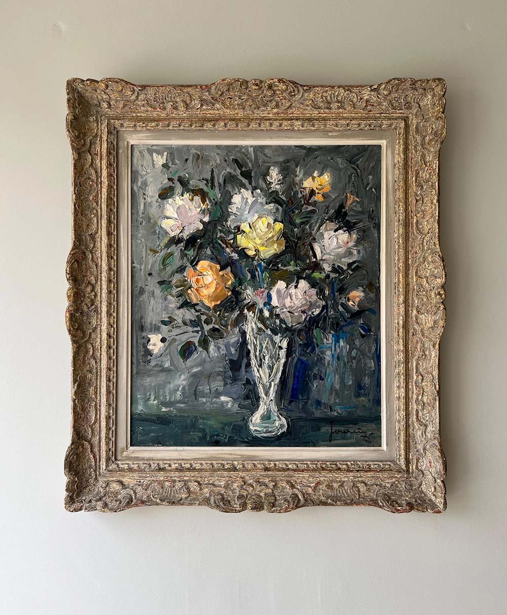 An ornate gold frame displays an oil painting of a glass vase holding white and yellow roses with green foliage, painted in a textured, impressionistic style on a dark background.
