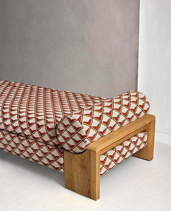 A modern wooden daybed with a geometric red and cream patterned cushion sits against a two-tone wall with gray and white sections.