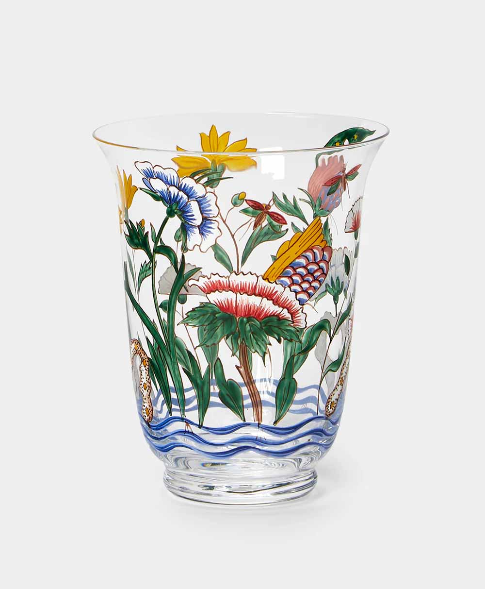 A clear glass vase decorated with colorful painted flowers, green leaves, butterflies, and blue wavy lines near the base. The vase has a flared rim and a rounded base, displayed against a plain light background.