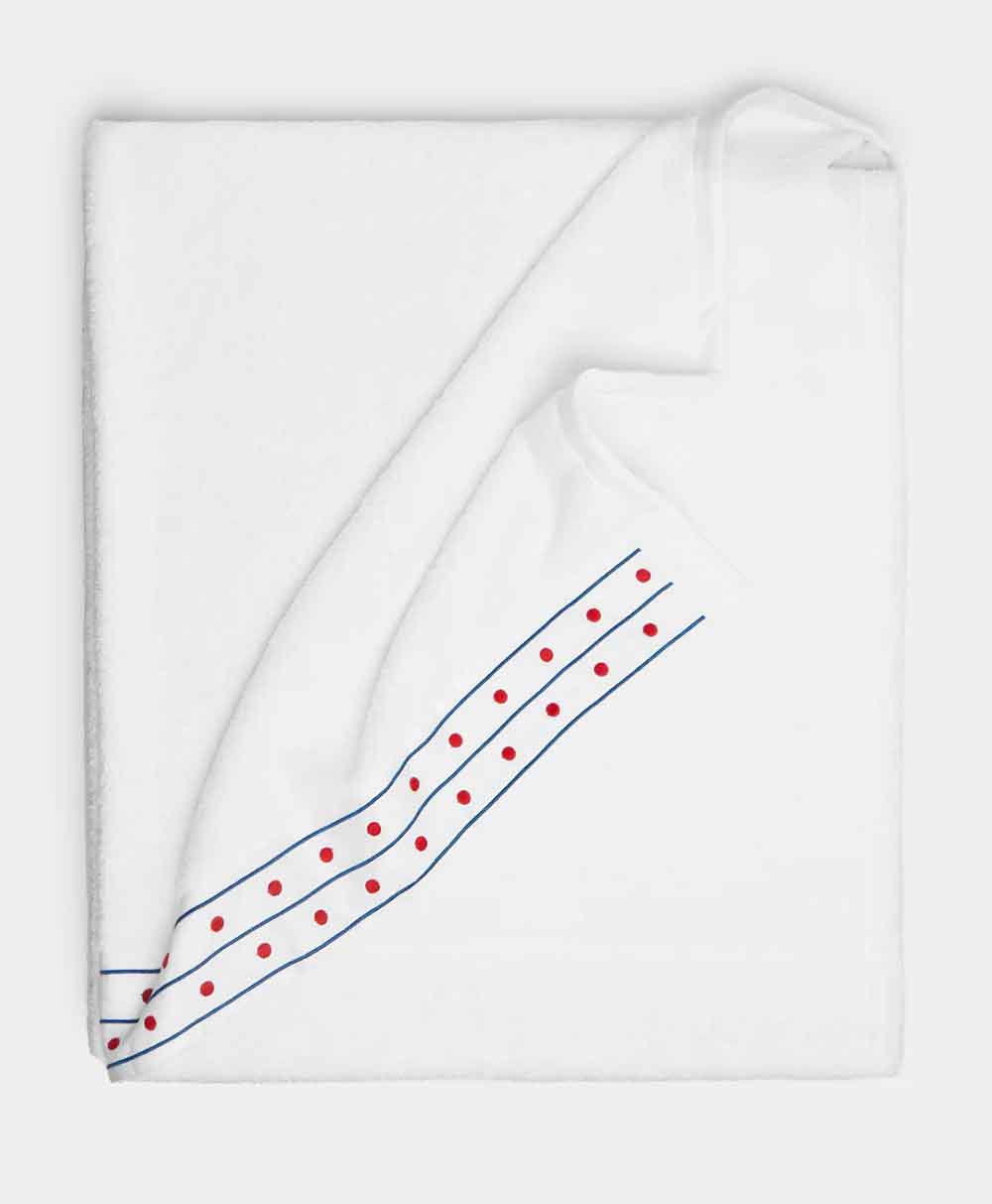 A neatly folded white towel with two thin blue stripes and a row of red dots along one edge, set against a plain light background.