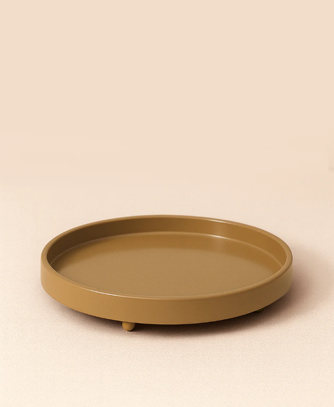 A round, shallow, mustard-yellow tray with a raised edge and small feet, placed on a neutral beige surface with a matching background.