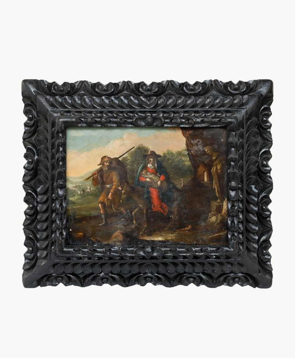 An ornate, dark carved wood frame surrounds a classical painting depicting two figures in historical attire outdoors, one seated and one standing with a staff, set against a landscape background.