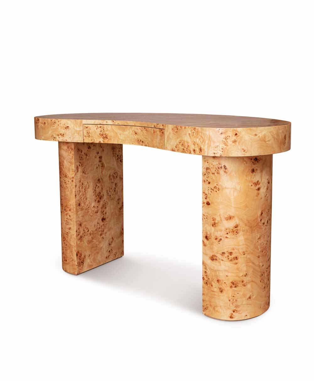 Curved desk made of light-colored wood with a unique burl pattern, featuring a rounded top, one rectangular leg, and one cylindrical leg, along with a slim central drawer.