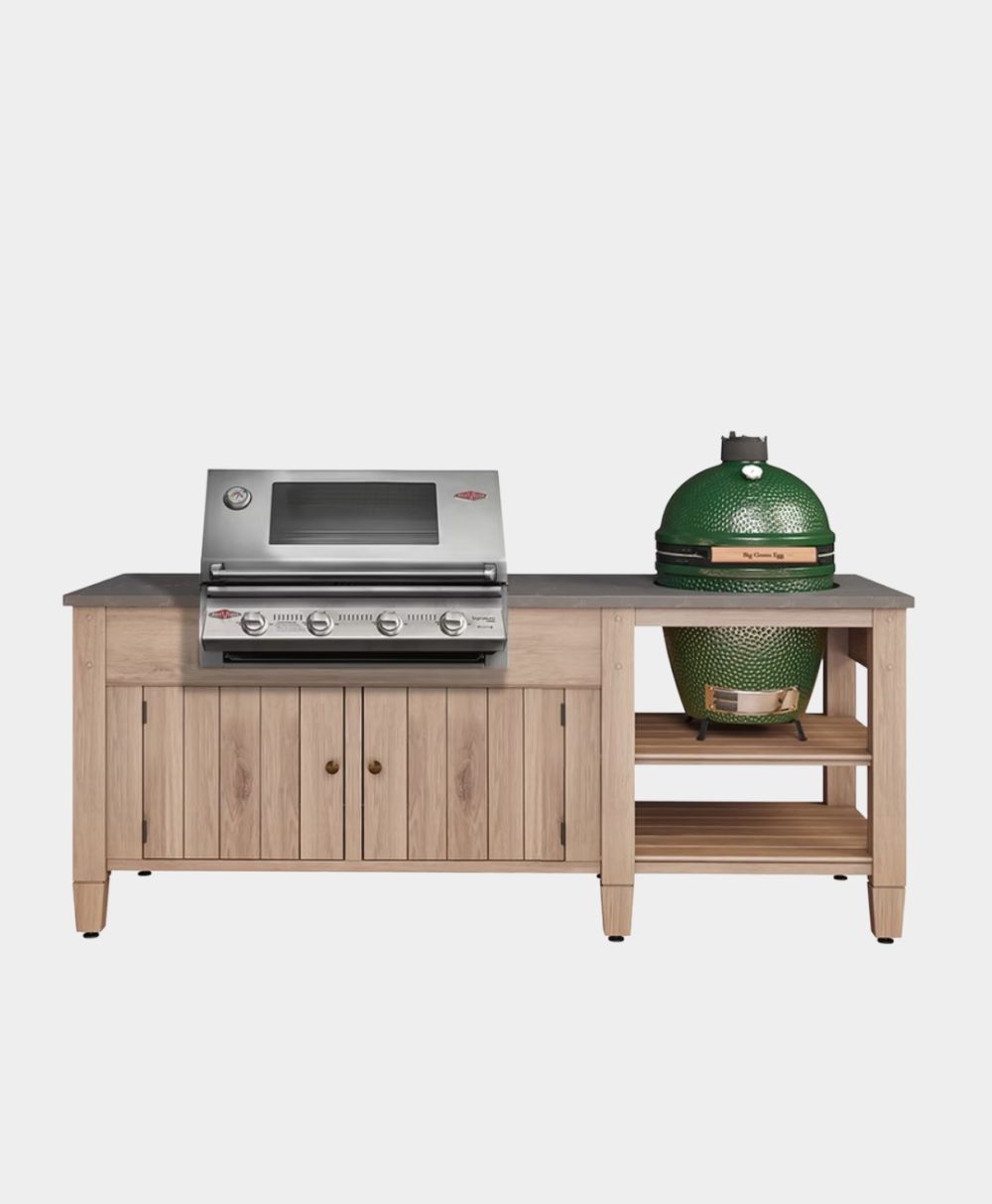 A wooden outdoor kitchen unit with a built-in stainless steel gas grill on the left and a green ceramic kamado-style grill on the right, featuring storage cabinets and open shelves underneath.