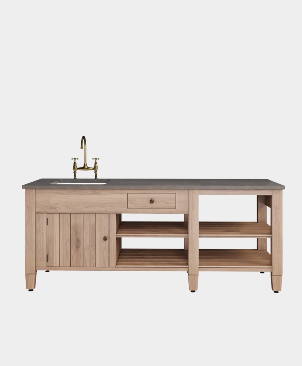A wooden kitchen island with open shelves, a single drawer, a cabinet, a dark countertop, an inset sink, and a brass faucet, set against a plain white background.