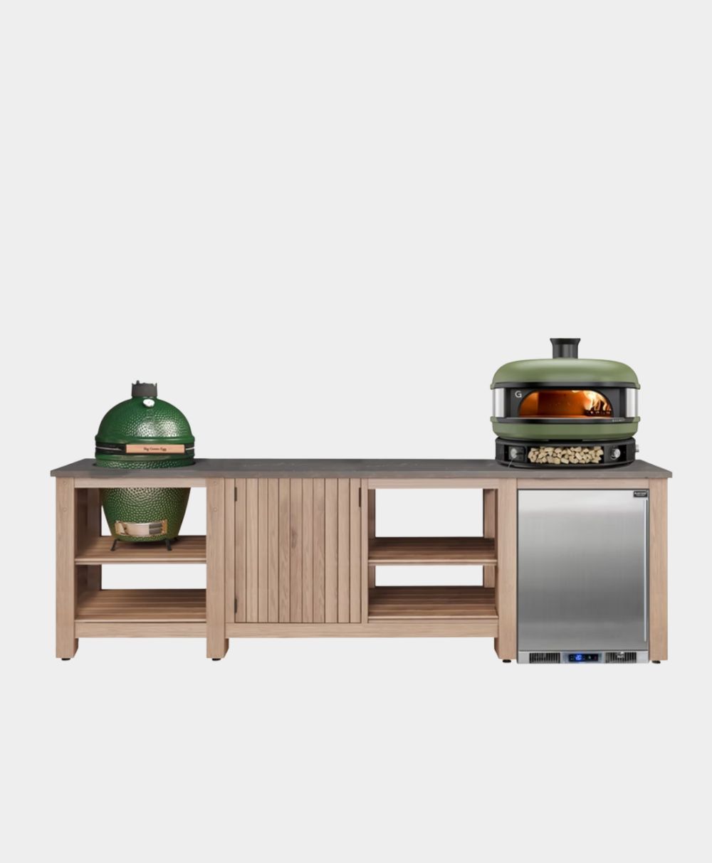 A modern outdoor kitchen station with a wooden base, featuring a green ceramic grill on the left, a pizza oven with fire visible on the right, and a stainless steel mini fridge below the oven.