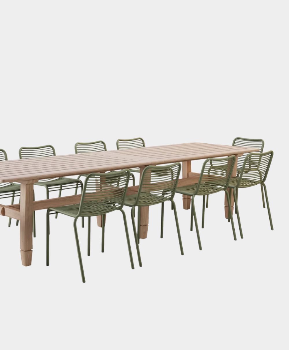 A long wooden dining table surrounded by eight green metal chairs with slatted backs and seats, set against a plain white background.