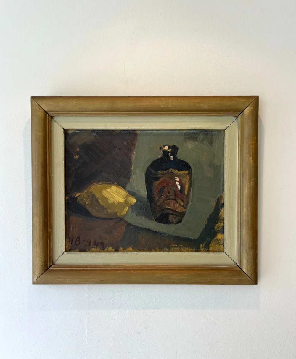 A framed painting of a dark vase and a yellow object on a table, set against a muted, abstract background. The artwork uses earthy tones and broad brushstrokes, and the frame is wooden with a light inner border.