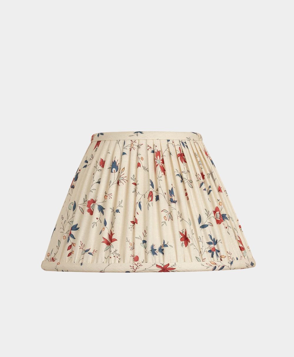 A cream-colored, pleated lampshade decorated with a delicate floral pattern in red, blue, and green on a white background.