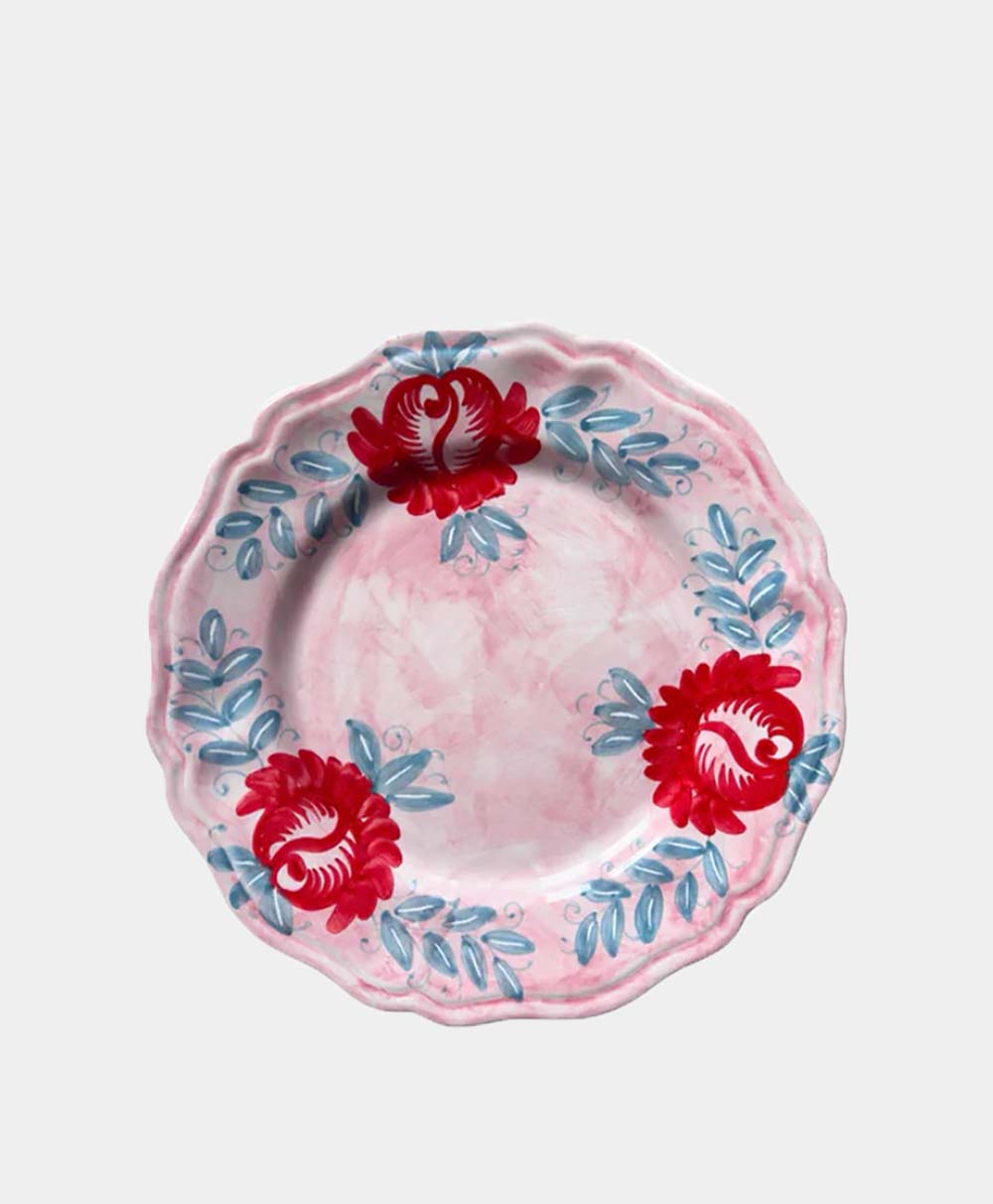 A round ceramic plate with scalloped edges, featuring a pink marbled background, two large red floral designs, and blue leafy accents around the rim.