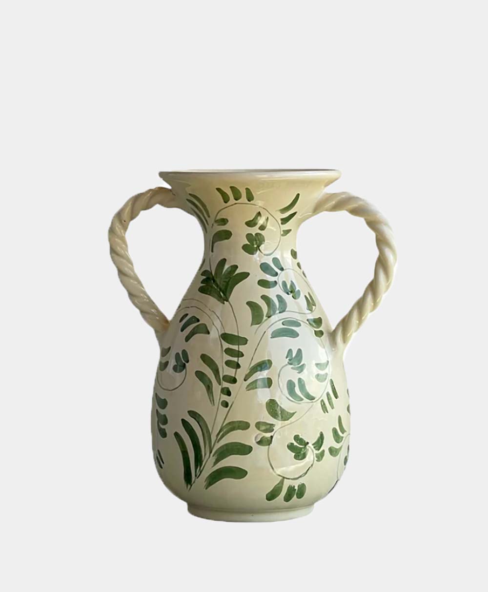 Cream-colored ceramic vase with two twisted handles and green leaf patterns painted on its surface, set against a plain white background.