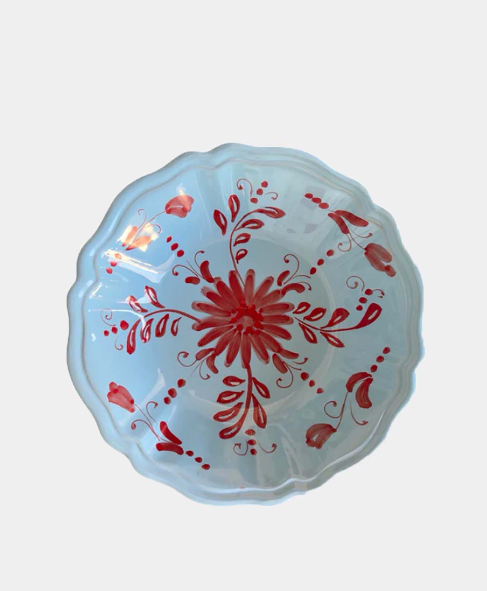 A round, scalloped-edge glass bowl with a light blue tint, decorated with a red floral and leaf pattern radiating from the center.