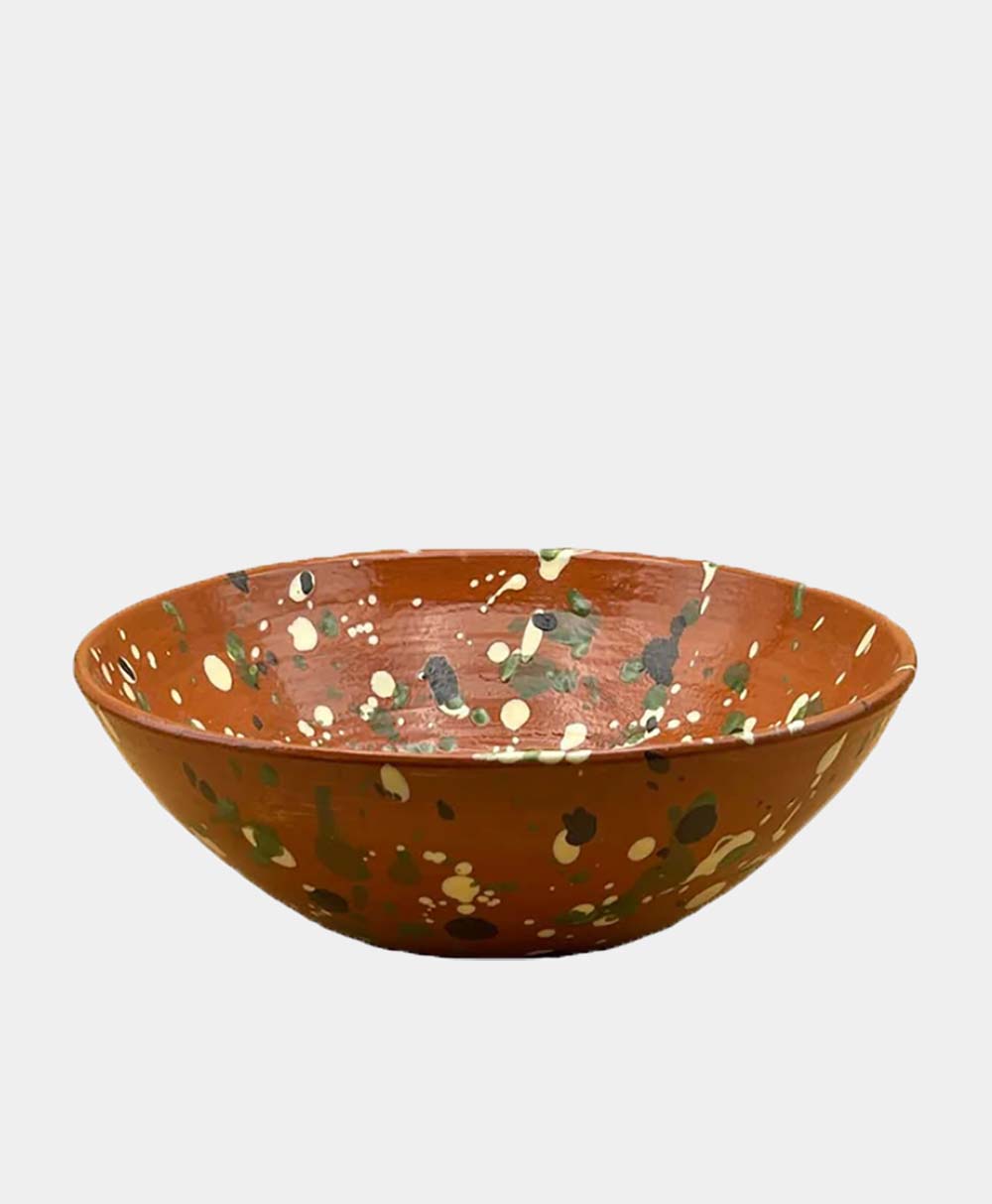 A shallow, round, brown ceramic bowl with a speckled pattern of cream, green, and dark spots on its surface, set against a plain white background.