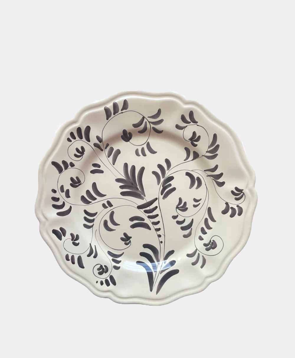 A white ceramic plate with a wavy edge, decorated with a swirling black floral and leaf pattern. The design appears hand-painted, giving the plate an elegant and artistic appearance.