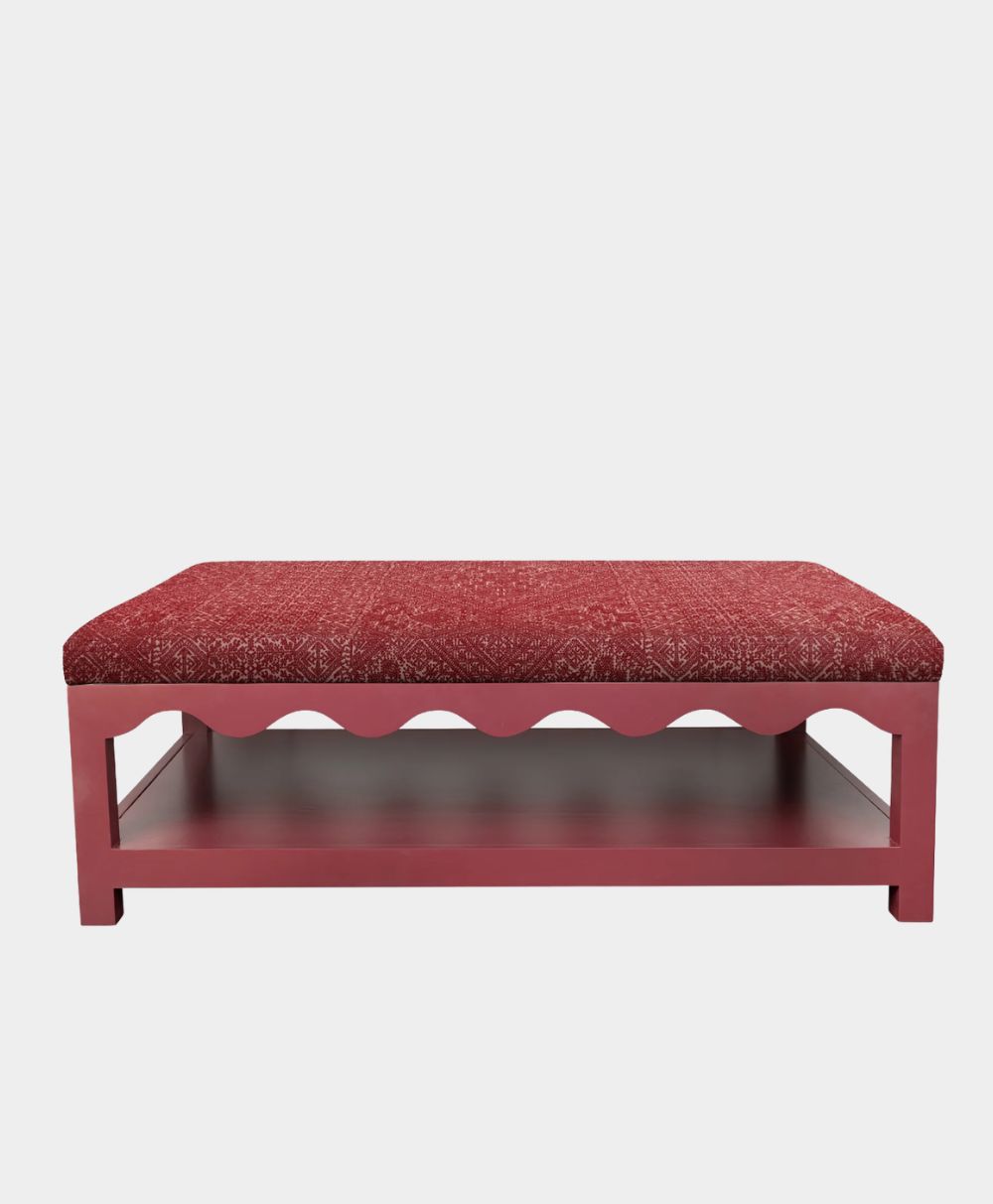 A rectangular red bench with a textured cushioned seat, scalloped apron detail, and an open lower shelf, set against a plain white background.
