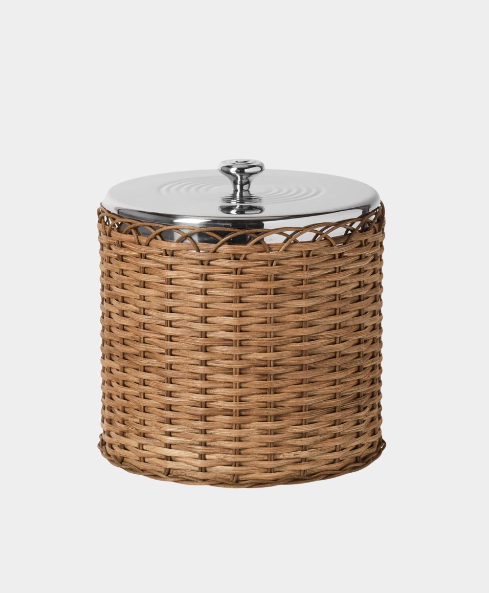 A round container with a woven rattan exterior and a shiny metal lid featuring a round handle, set against a plain white background.