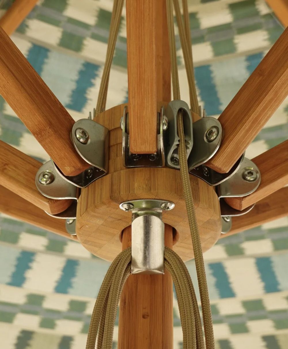 Close-up view of the wooden and metal central hub mechanism of an umbrella, showing spokes, bolts, and fabric canopy with a blue and white patterned design in the background.