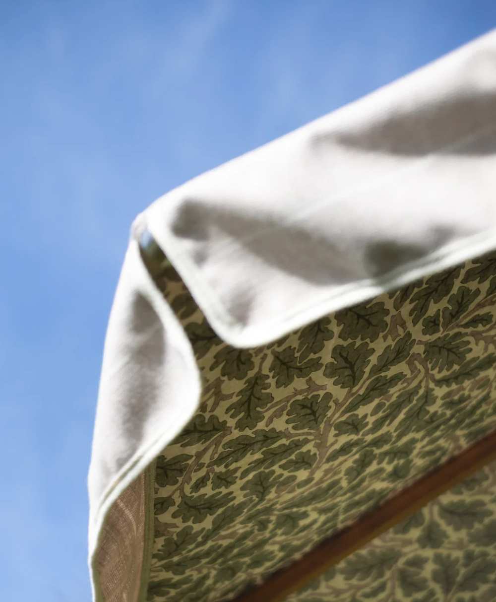 Close-up of the edge of a fabric canopy or umbrella, with a leafy green pattern on the underside and a plain light-colored top, set against a blue sky.