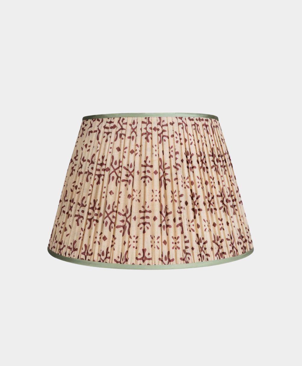A pleated lampshade with a beige background and a maroon floral pattern, trimmed with muted green edges, set against a plain white background.