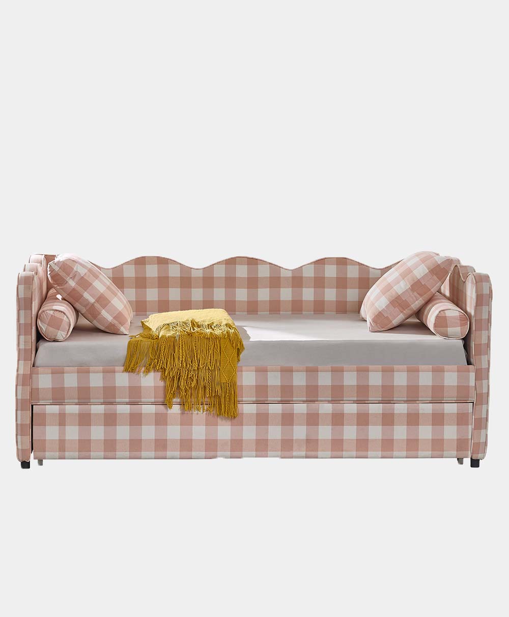 A pink and white gingham daybed with a scalloped back, two round bolster pillows, two square pillows, and a yellow fringed throw blanket draped over the seat.