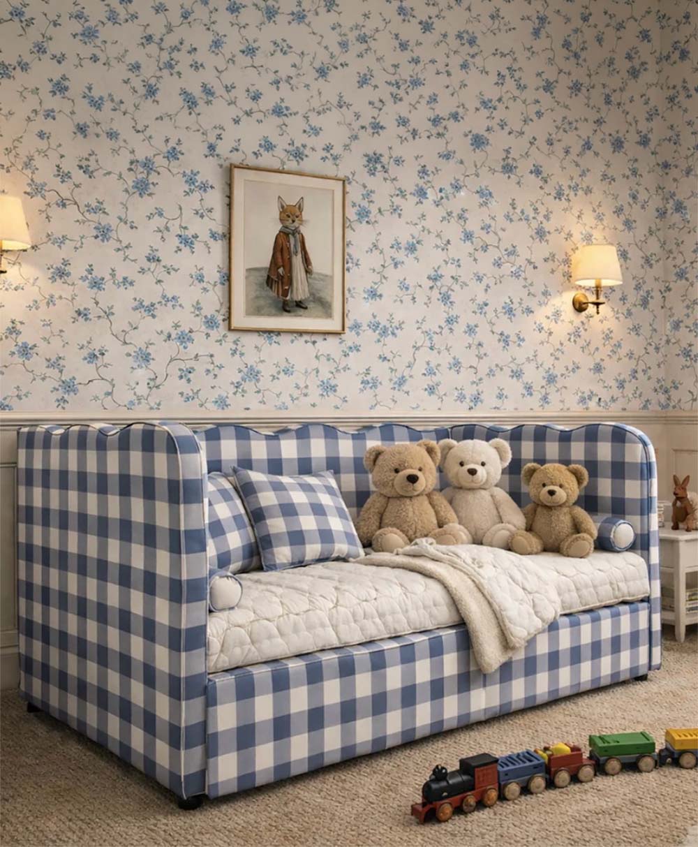 A cozy kid’s room features a blue and white checkered daybed with three teddy bears, a plaid cushion, soft bedding, toy trains on the floor, floral wallpaper, two wall lamps, and a framed fox illustration above the bed.