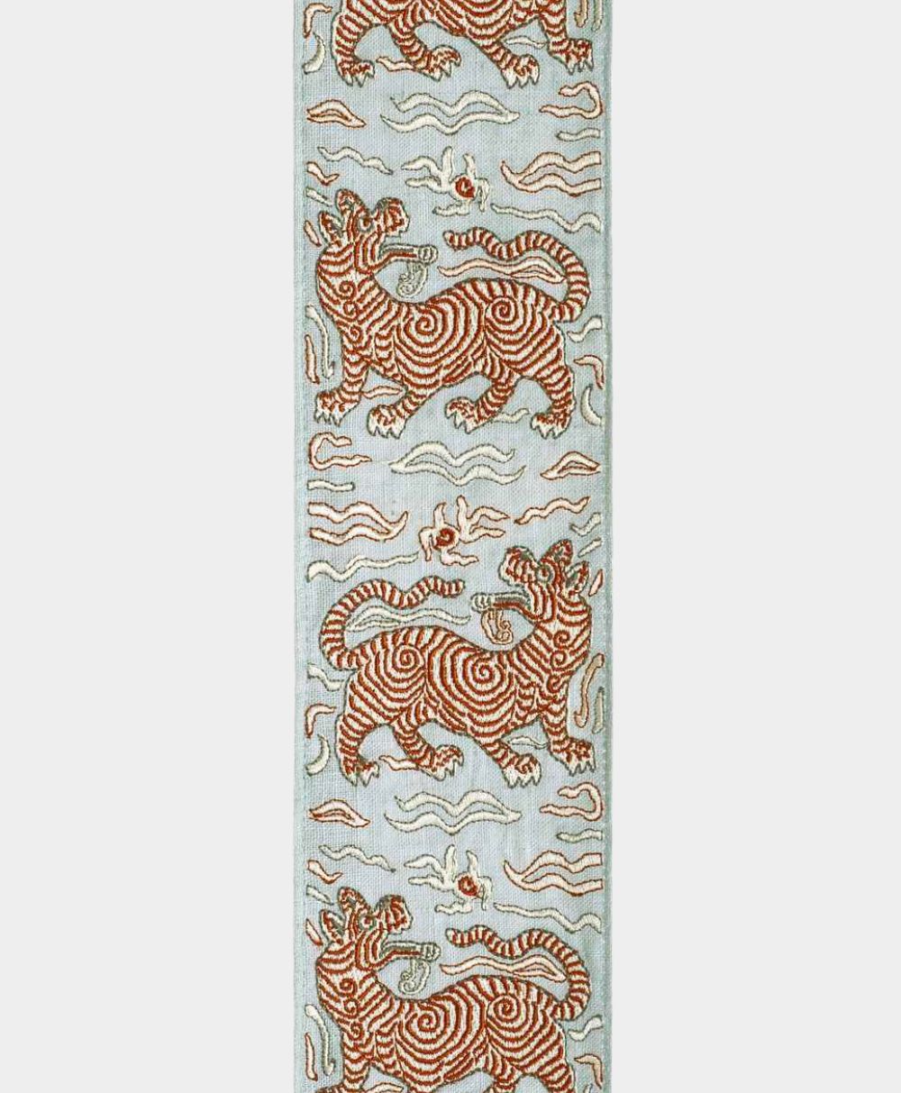 A vertical fabric strip featuring repeating embroidered red and gold striped tigers with open mouths, surrounded by stylized clouds and a pale blue background.