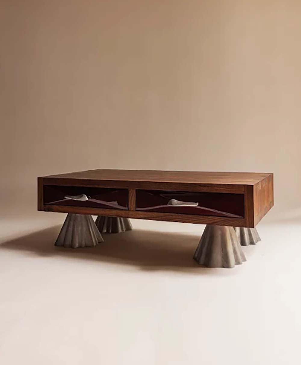 A modern wooden coffee table with two drawers, each featuring sculptural handles, stands on four wide, conical metal legs. The background is plain, highlighting the tables unique design.