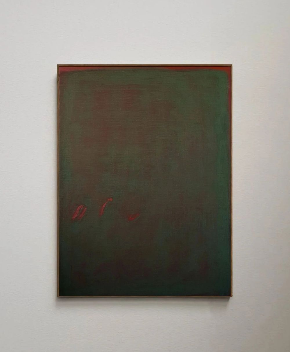 A rectangular painting with a dark, muted green and brown background. Three small red brushstrokes appear in the lower left area. The artwork hangs on a plain white wall.