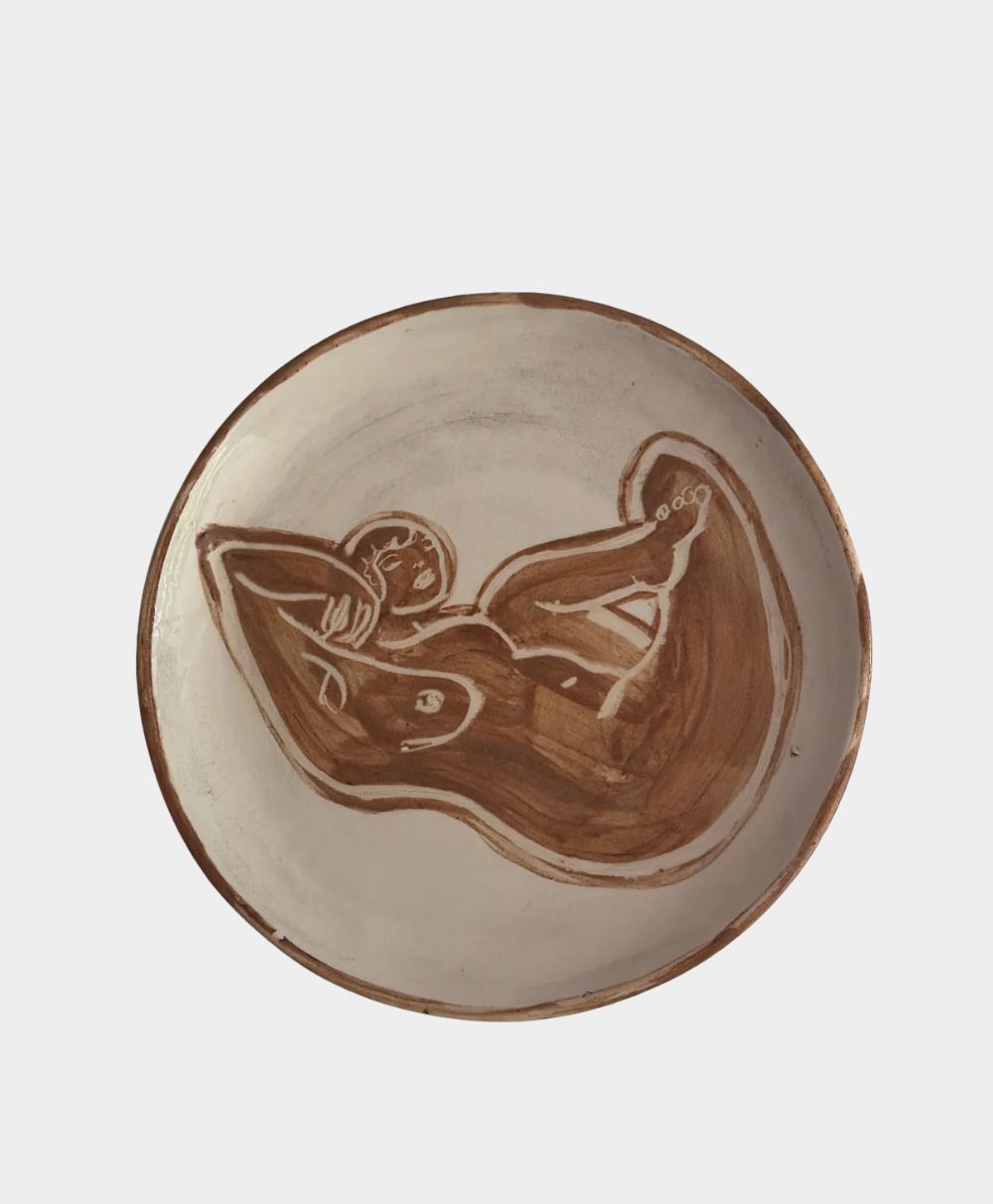 A ceramic plate featuring a brown, abstract line drawing of a reclining nude figure against a light, off-white background.