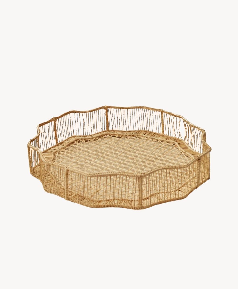 A round, shallow woven basket with wavy edges and an open, airy design made from natural-colored material, displayed on a plain white background.