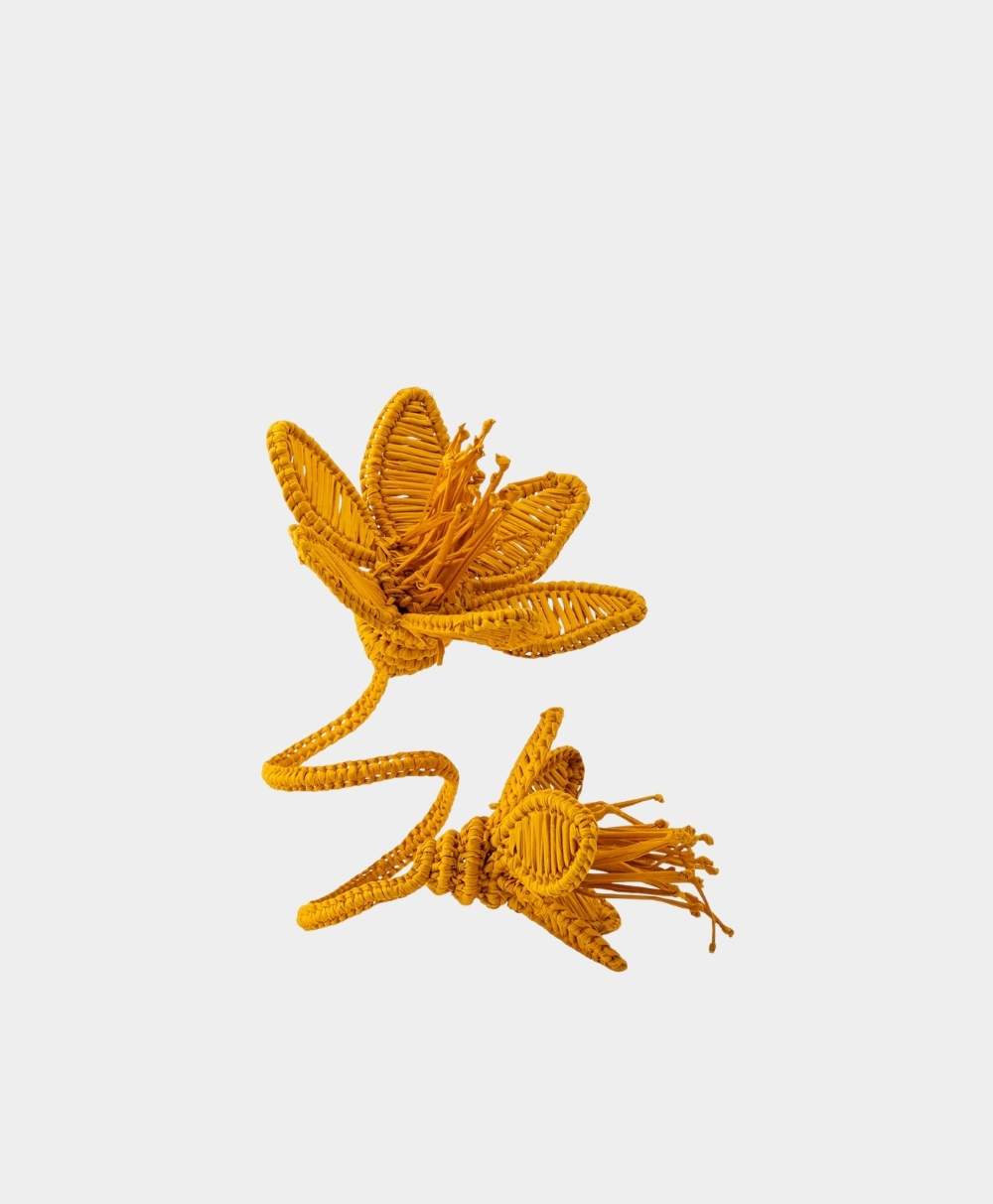 A decorative ring made of woven yellow material shaped like two flowers, with detailed petals and stamen, set against a plain white background.