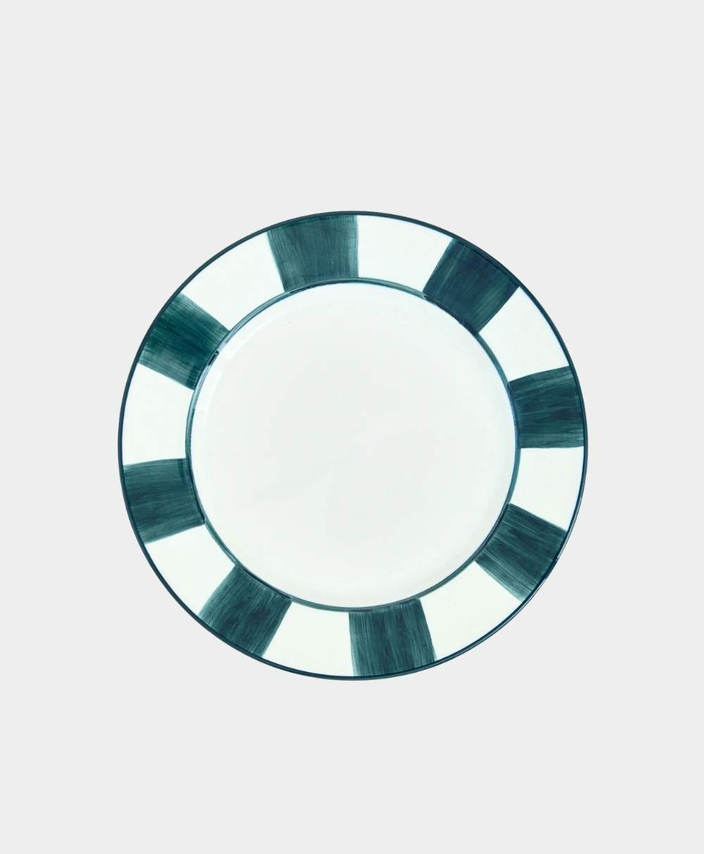 A round ceramic plate with a white center and a border featuring alternating wide, dark green and white segments. The plate is placed on a plain, light gray background.