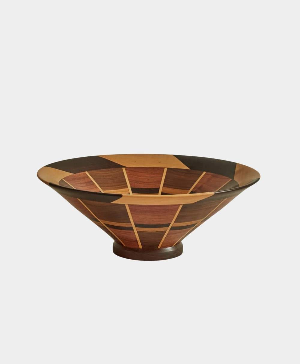 A wide, shallow wooden bowl with a geometric, segmented pattern in various shades of brown and tan, set against a plain white background.