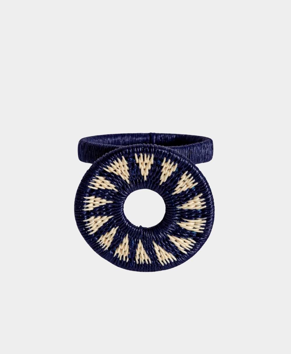 A ring featuring a circular, woven design in navy blue and cream, with a central hole and geometric pattern radiating outward, displayed on a plain light background.