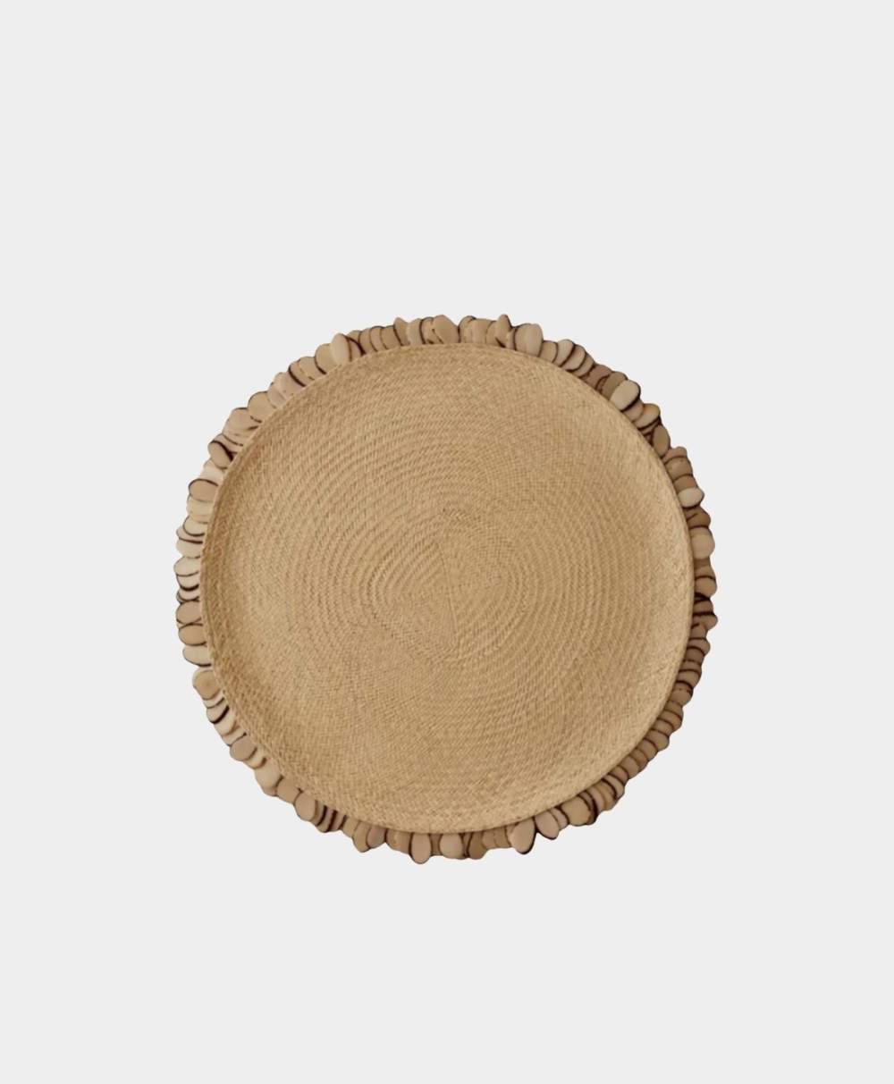 A round, woven straw tray with a decorative border of smooth, oval-shaped beige stones around the edge, displayed on a plain white background.