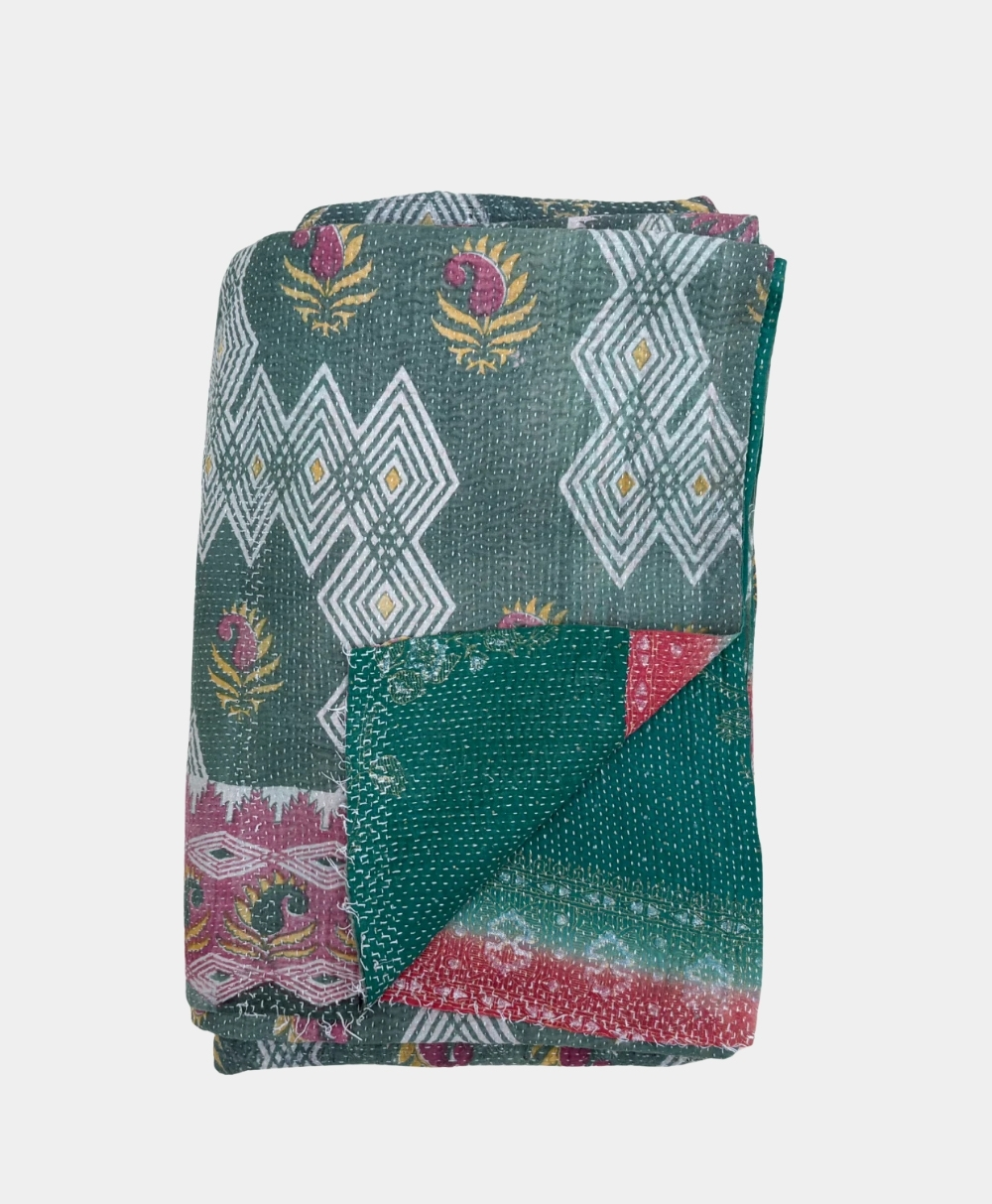 A folded green textile with white geometric patterns, yellow and red floral motifs, and a border featuring red and pink accents. The reverse side shows a teal and red section with small white dots.